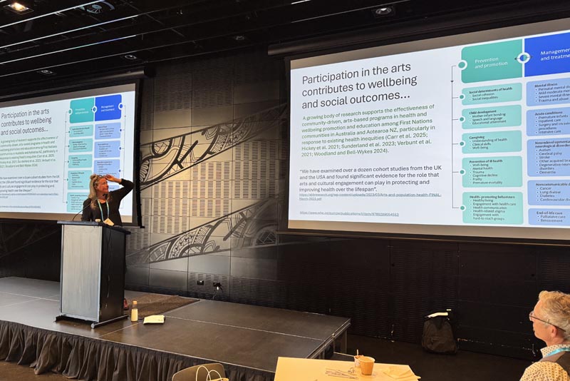 Molly Mullen behind a lectern, hand to forehead and looking at her slides on a large screen behind her